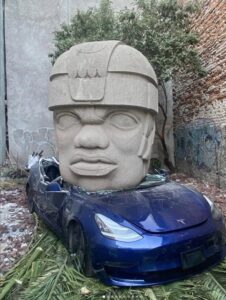 Installation (2024) by Chavis Mármol from his 'NEO-TAMEME' series, consisting of a stone sculpture crushing a Tesla car